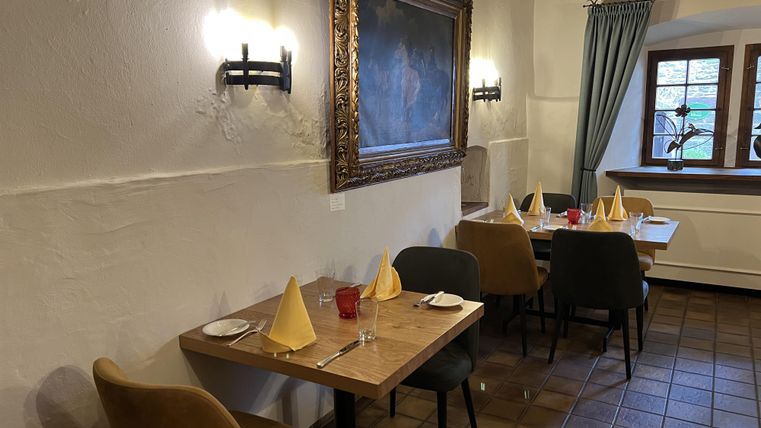 Un restaurant cozy avec des tables en bois et des nappes élégantes.
Un grand tableau est accroché au mur, et la lumière douce passe par la fenêtre.