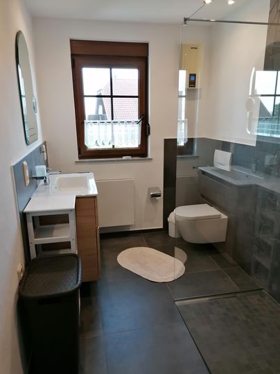 Ein modernes Badezimmer mit einer Dusche und einem eleganten Waschbecken. Große Fenster sorgen für viel Tageslicht.