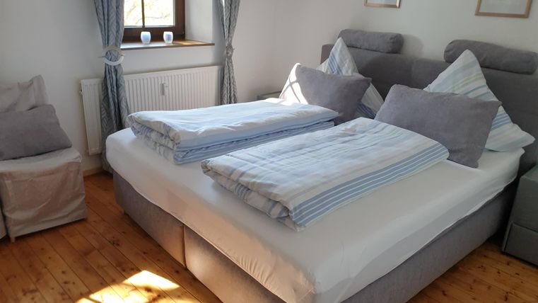 Une chambre confortable avec un grand lit double et des rideaux clairs. Le sol est en parquet et il y a des tableaux décoratifs sur les murs.