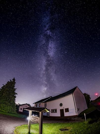 A clear night sky with the Milky Way above the holiday home. Surrounded by trees and gentle landscapes, the scene exudes tranquility and beauty.