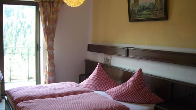 Une chambre confortable avec deux lits séparés et des oreillers à carreaux. Une fenêtre donnant sur un balcon laisse entrer la lumière du jour.