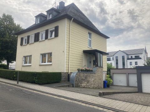 Une maison de deux étages avec une façade jaune clair et un toit sombre. Elle se trouve dans une rue calme avec quelques bâtiments voisins.