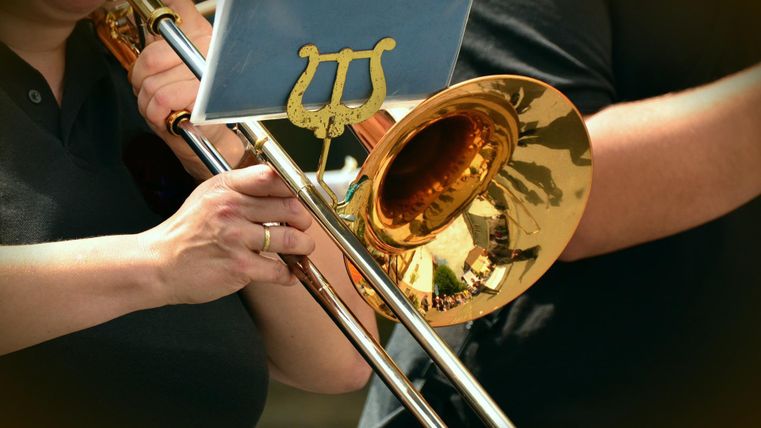 Eine Person spielt eine glänzende Posaune. Im Hintergrund sind weitere Musiker zu sehen.