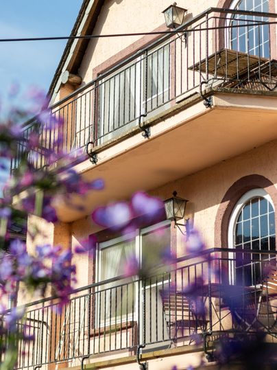 Ein hübsches Gebäude mit Balkonen und großen Fenstern. Im Vordergrund sind violette Blüten zu sehen.