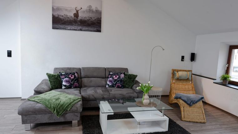 Un salon confortable avec un canapé gris et des coussins colorés. Une table en verre et un fauteuil complètent le décor moderne.
