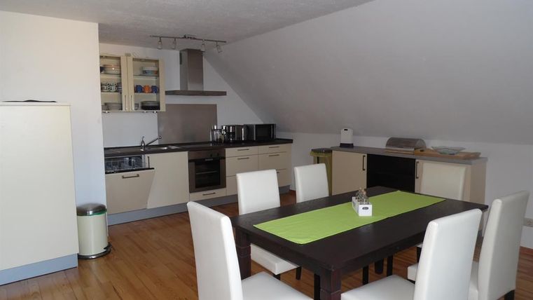 Moderne keuken met elegante meubels en een grote eettafel. De ruimte is licht en vriendelijk met een houten vloer en hoogwaardige apparaten.