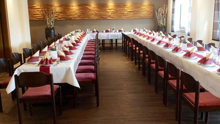 Une salle de réception élégante avec de longues tables joliment dressées. Des serviettes rouges et une décoration raffinée créent une ambiance accueillante.