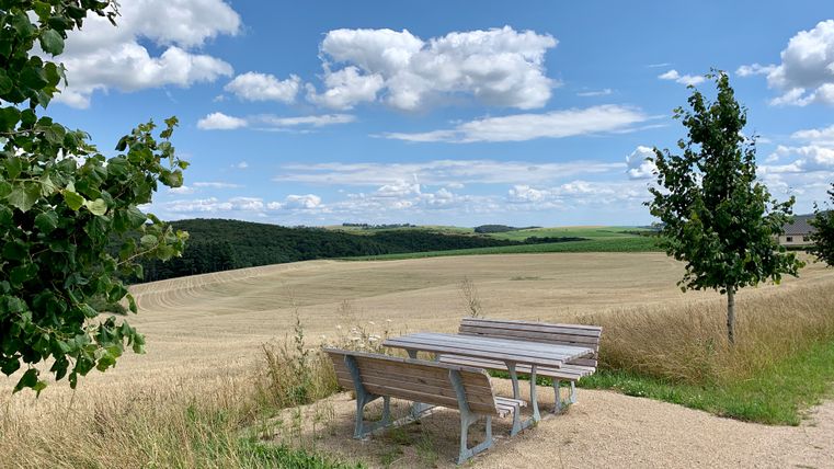Eine Holzsitzgruppe mit Ausblick auf die trockenen Felder und die Waldstücke