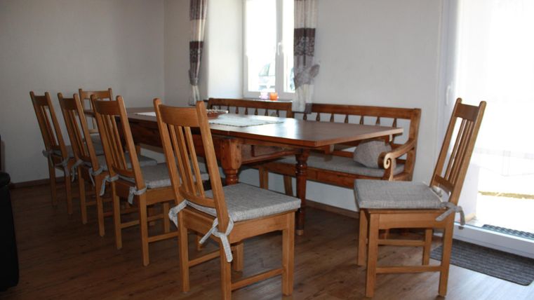 Ein gemütlicher Essbereich mit einem großen Holztisch und vielen Stühlen. Das Zimmer hat einen hellen, einladenden Charakter und große Fenster.