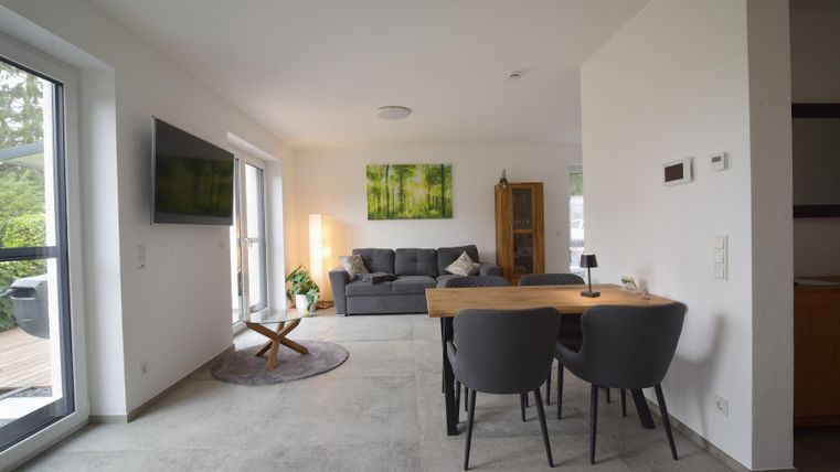 Een moderne woonkeuken met een gezellige bank en een eettafel. Heldere muren en grote ramen zorgen voor veel licht.