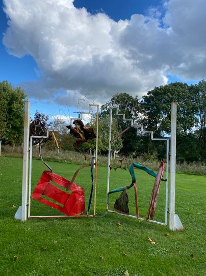 Metallskulptur auf einer Wiese mit Wolken im Hintergrund.