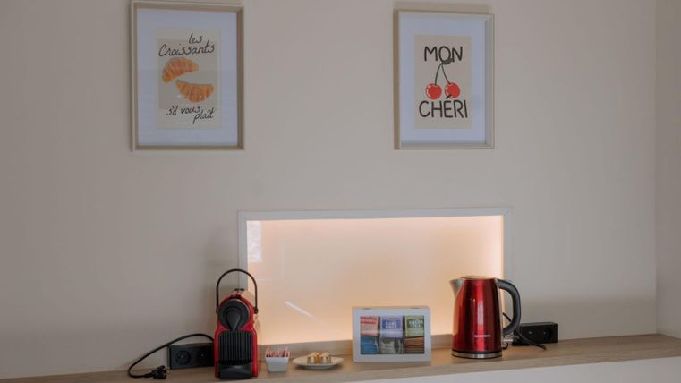 Eine gemütliche Nische mit einem Wasserkocher, einer Kaffeemaschine und einer kleinen Auswahl an Tees. An der Wand hängen zwei Bilder mit französischen Schriftzügen.