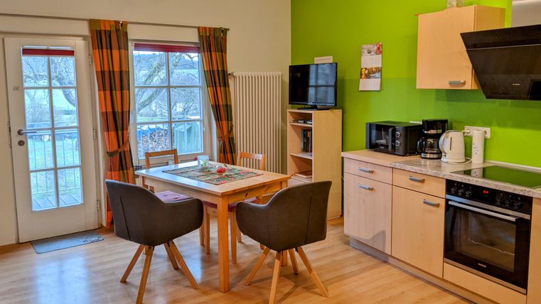 Eine moderne Küche mit einem runden Tisch und bequemen Stühlen. Die Wände sind in einem frischen Grünton gestrichen, und es gibt große Fenster mit Vorhängen.