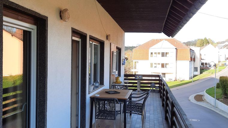 Ein großzügiger Balkon mit einem Tisch und Stühlen. Im Hintergrund sind Häuser und eine ruhige Straße sichtbar.