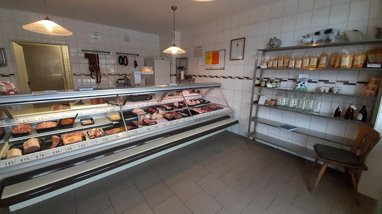 A butcher shop with a counter full of fresh meat products. In the background, there are shelves with various products and a seating area visible.