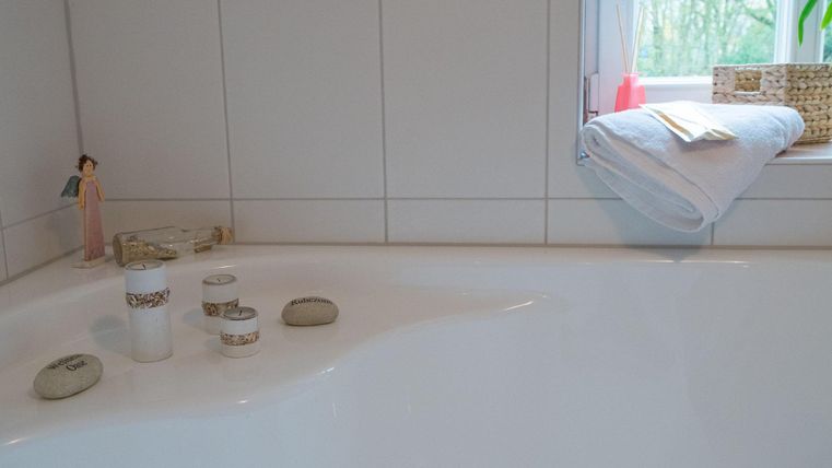 Een badkamer met een wit bad en enkele decoratieve elementen. Op de vensterbank liggen handdoeken en kleine accessoires.