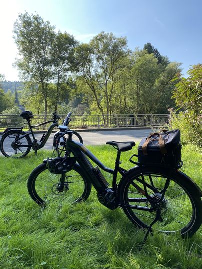 Deux vélos sont au premier plan sur de l'herbe verte. En arrière-plan, on peut voir des arbres et un ciel dégagé.
