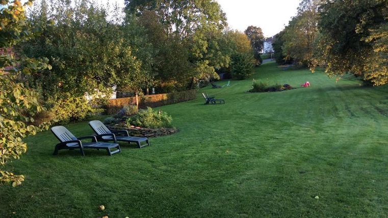 Un jardin bien entretenu avec une pelouse verte et des arbres. Au premier plan, deux chaises longues pour se détendre.