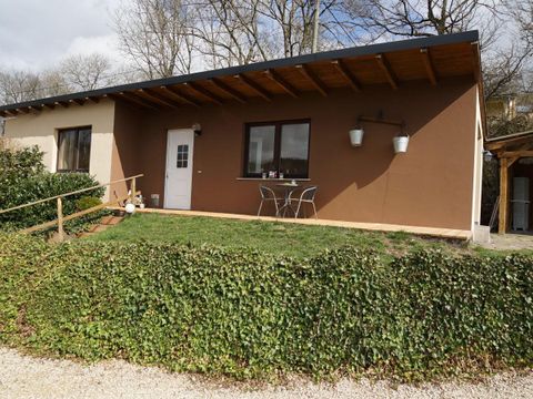Une maison individuelle moderne avec une terrasse et deux chaises. Le terrain est verdoyant avec des haies basses et une surface en gravier.