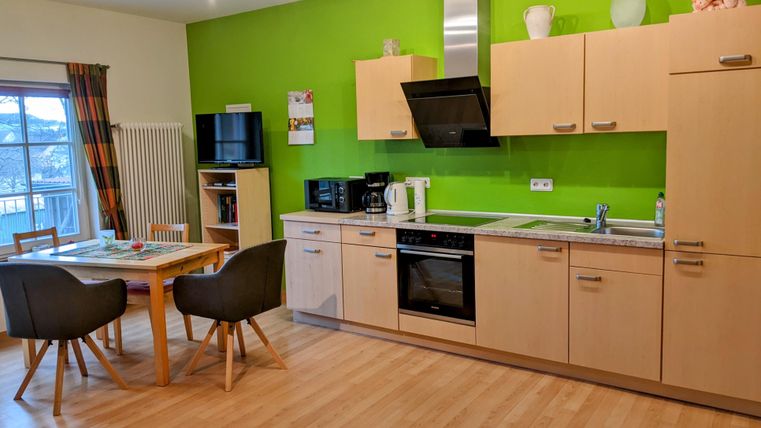 Eine moderne Küche mit grünen Wänden und Holzregalen. Der Essbereich ist mit einem Tisch und Stühlen ausgestattet.