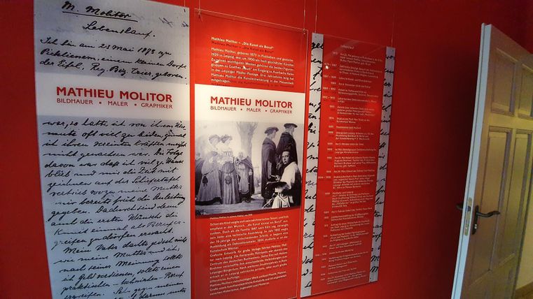 A wall with information about Mathieu Molitor, including handwritten texts and photos. The wall is painted red and showcases various exhibits.