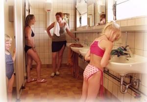 Une cabine d'essayage lumineuse avec plusieurs personnes en maillot de bain. Deux femmes discutent, tandis qu'une fille se tient au lavabo.