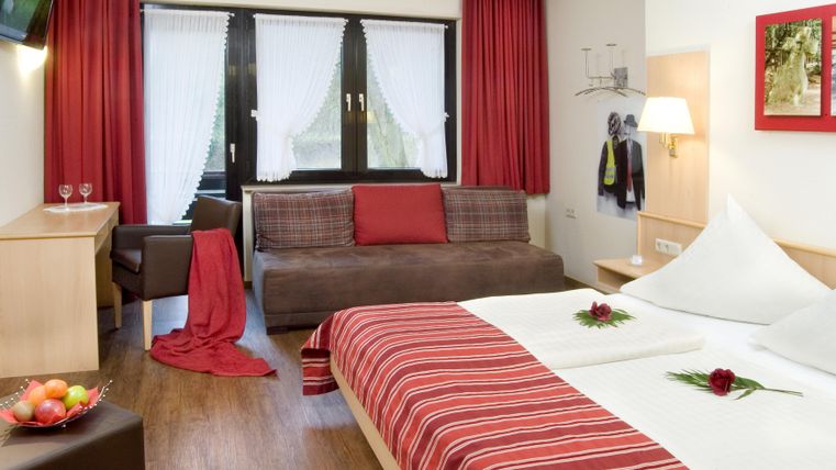 Une chambre moderne avec un lit double et un canapé confortable. Les murs sont peints dans des tons chauds, et une table avec des fruits frais est prête.