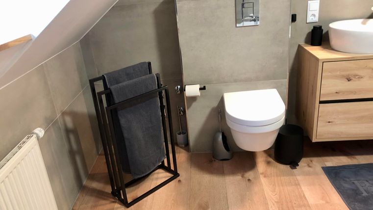 A modern bathroom with minimalist decor. Wooden floorboards are laid on the floor, and there is a toilet as well as a washbasin.