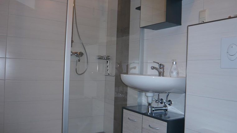 Une salle de bain moderne avec une douche, un lavabo et des toilettes. Les murs sont carrelés en clair et le mobilier est simple et élégant.