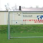 Een voetbaldoel op een groen speelveld. Op de achtergrond is een gebouw te zien met de tekst "Sportschool Bitburg".