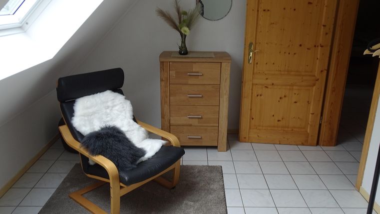 Une pièce confortable avec un fauteuil et un tapis doux. À côté du fauteuil se trouve une commode et un miroir est accroché au mur.