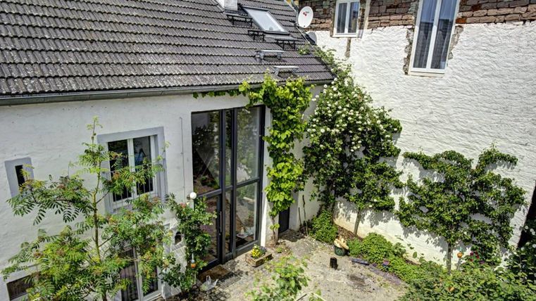 Een charmant, lichtovergoten huis met een glasgevel en groene begroeing. De kleine tuin is versierd met planten en bomen die een uitnodigende sfeer creëren.