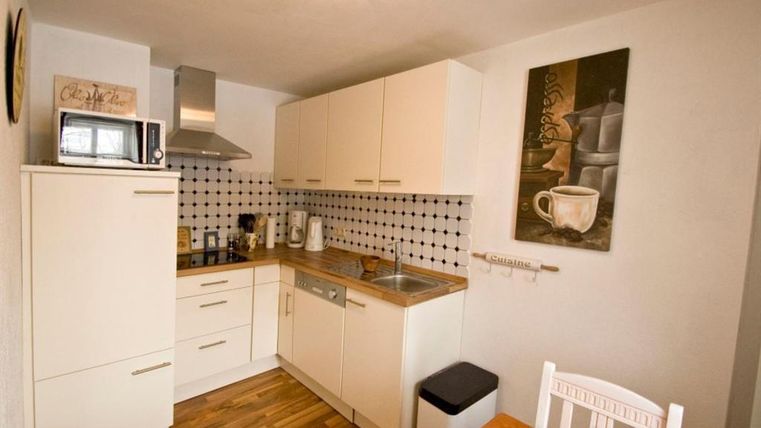 Een moderne keuken met lichte kasten en een houten vloer. De inrichting omvat een fornuis, een gootsteen en een eettafel.