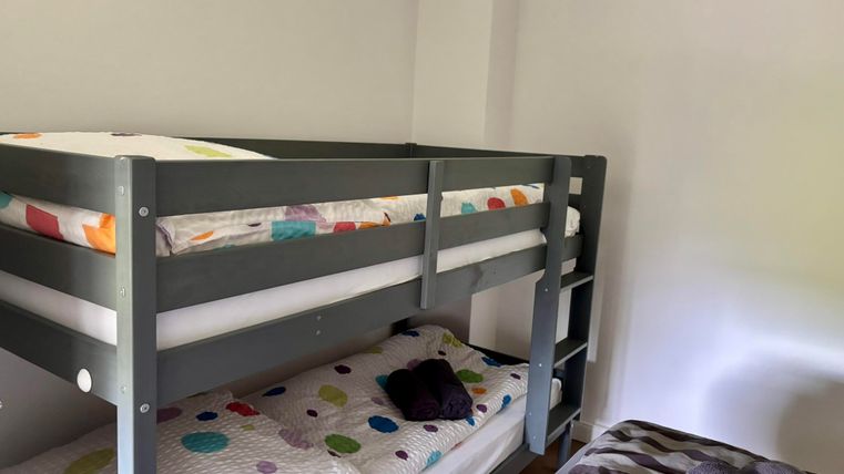 Ein Kinderzimmer mit einem Etagenbett und einem Einzelbett. Die Bettwäsche hat bunte Muster auf weißem Grund.