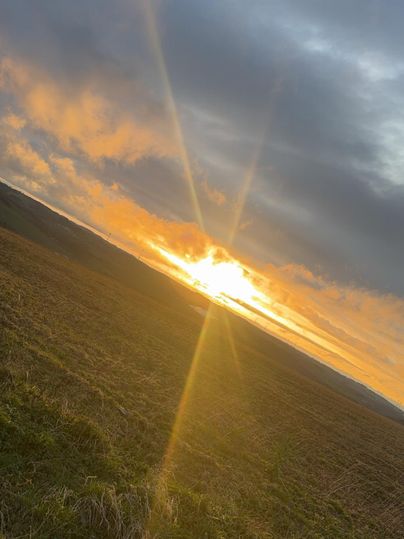 Ein wunderschöner Sonnenuntergang über einem Feld. Der Himmel ist mit Wolken und warmen Farben gefüllt.