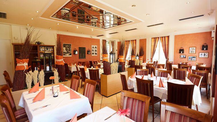 Ein gemütliches Restaurant mit eleganter Einrichtung. Die Tische sind mit weißen Tischdecken und orangefarbenen Servietten gedeckt.