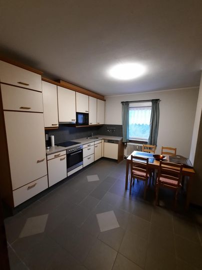 Eine moderne Küche mit hellen Möbeln und einem Esstisch. Das Zimmer hat ein großes Fenster und eine freundliche Atmosphäre.