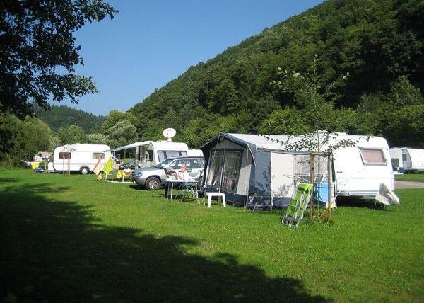 Un camping pittoresque avec des camping-cars et des caravanes sur une pelouse verte. En arrière-plan, on peut voir des collines douces et des arbres.