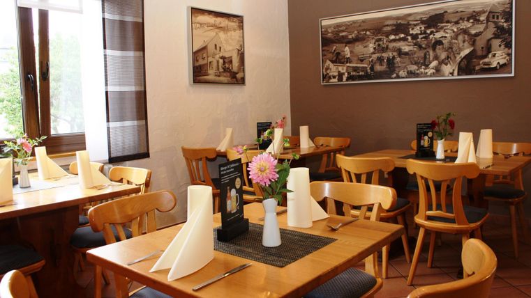 Un restaurant accueillant avec des tables et des chaises en bois. Des vases avec des fleurs et des nappes fraîches créent une atmosphère agréable.