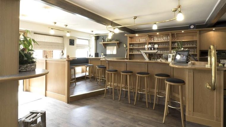 Een moderne bar met houten meubels en hoge zitplaatsen. De inrichting is licht en uitnodigend, ideaal voor gezellige bijeenkomsten.