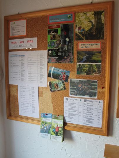 Een prikbord met informatie en flyers over lokale aanbiedingen. Er zijn verschillende posters en lijsten zichtbaar.