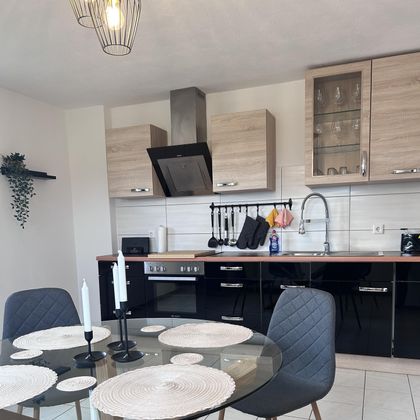 Een moderne keuken met houten en zwarte keukenkasten. Een ronde eettafel met witte placemats en stoelen is ook aanwezig.