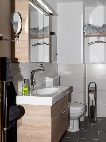 Ein modernes Badezimmer mit Holzschränken und einem eleganten Waschbecken. Die Wände sind hell gefliest und es gibt praktische Ablagen.