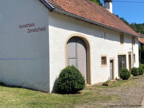 An art house with a white façade and a red roof. The entrance is decorated with a large wooden door and small bushes.