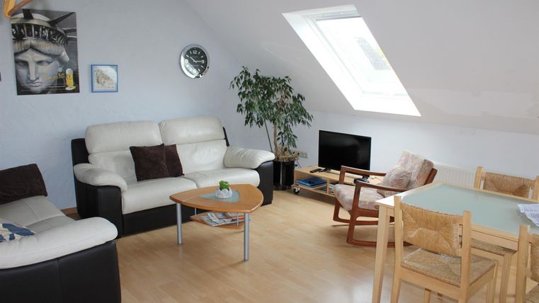 Een gezellige woonkamer met een lichte inrichting. Er is een bank, een eettafel en veel daglicht door een dakraam.