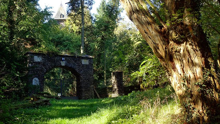 Steinbogen im Wald mit Turm im Hintergrund, umgeben von Bäumen.