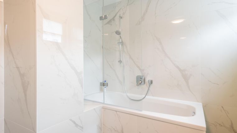 Une salle de bain moderne avec une baignoire et des murs élégants en marbre. La lumière vive crée une atmosphère accueillante.