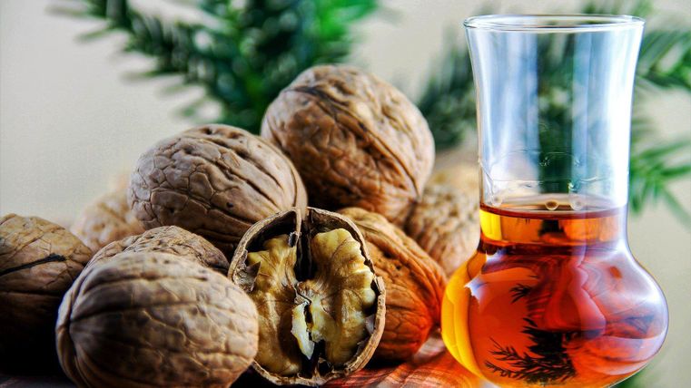 Een glas met een donkere drank staat naast een groep walnoten. Op de achtergrond zijn groene bladeren zichtbaar.