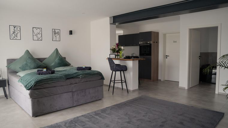 Ein modernes Schlafzimmer mit einem großen, bequemen Bett und eleganter Dekoration. An einer kleinen Bar stehen Stühle und es gibt eine gepflegte, offene Küchenzeile.