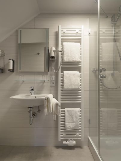 Ein modernes Badezimmer mit einem Waschbecken, einem Spiegel und einem Handtuchwärmer. Die dusche ist in einem eleganten, klaren Design gehalten.